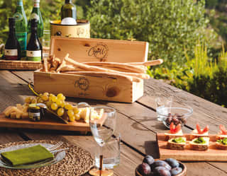 Golden grissini overflow from a wooden wine box next to platters of cheese, grapes and canapés. White wine cools in buckets
