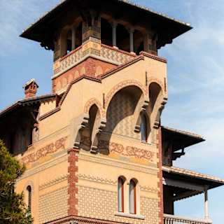 Low-angle view of Villa Beatrice with geometric decoration, external staircase, multiple balconies, and a whimsical torretta.