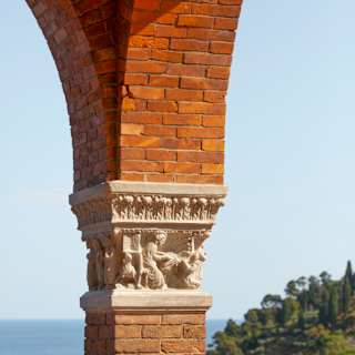 Close-up of a carved stone element on the brickwork of an arched balcony support with iron railings and incredible bay views.