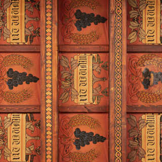 Close-up of a handpainted panel with a repeat sequence of bunches of grapes and scrolls, divided by decorated wood pieces.