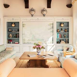 A glass door spills light into Villa Beatrice's living room with a sofa, bench, two armchairs, artwork and elegant shelving.