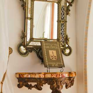 A book about Tuscan architect Gino Coppedè rests on a marble-topped shelf below an ornate gilt-framed Venetian-style mirror.