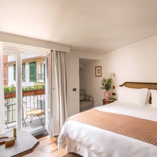 Light and airy hotel suite with parquet flooring, king bed and plush chair in small nook
