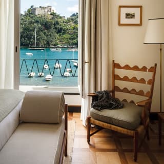 Suite interior with a chair and an open window with a view of boats on Portofino Bay