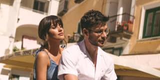 Glamorous couple on a vespa driving across the sunny piazzetta of Portofino