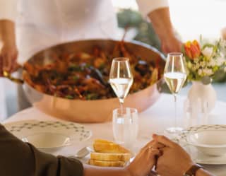 A couple holds hands as the chef serves a dish tableside