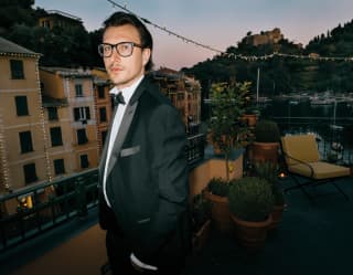 A dark haired young man in black tie and dark-rimmed glasses gazes impassively at the camera on the Ava Gardner Terrace