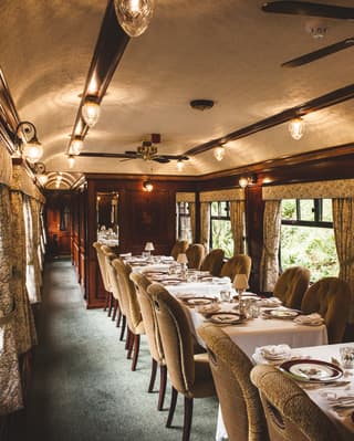 Tables-for-four lining a wood-panelled dining car with elegant window drapes
