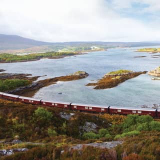 Burgundy train carriages curving alongside a rugged loch dotted with little islands