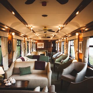 Lamplit train observation car with plush tweed and tartan sofas and armchairs