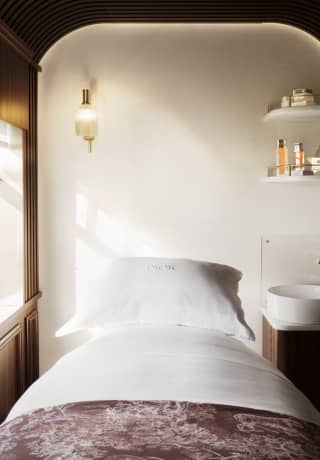 Inside a serene Dior Spa treatment room, with a fresh white bed, sink and shelves of products, cocooned in cedar panelling.>