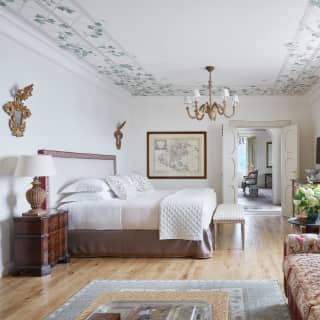 Two rococo wall mirrors, chandelier and period pieces marry with white bed and walls for fresh elegance in Miramare Suite.