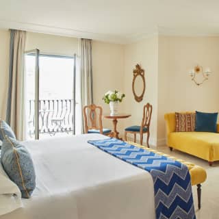 This bedroom feels joyful, with indulgent yellow velvet chaise and ottoman, marble floors and bright blue fabric accents