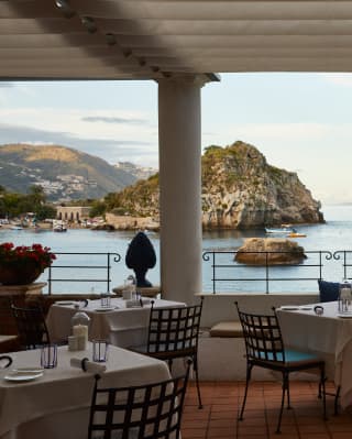 Boats bob in the bay across the dining terrace balcony, the setting sun turning the terrace's columns into silhouettes