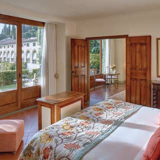 Enormous windows give a pink velvet bedroom chair amazing views of the gardens, villa walls and row of tall Cypress trees