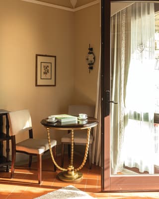 Two espresso cups and an artbook sit on a polished circular table in the corner of terracotta tiled room