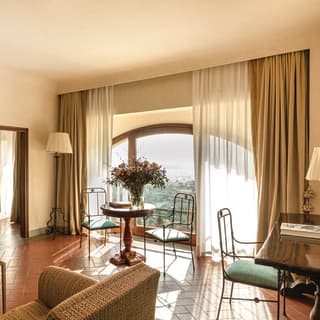 Sun glows behind drapes half-covering the arched window of Limonaia, with honey walls, terracotta tiles and simple furniture.
