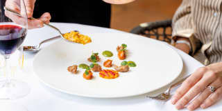 A hand spooning saffron risotto onto a white plate topped with starter-style bites