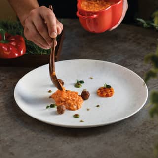 Chef Cozzolino spoons Carnaroli risotto with capsicum and sausage from a red bell-pepper-shaped dish on to a white plate.