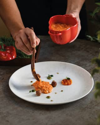 Chef Cozzolino spoons Carnaroli risotto with capsicum and sausage from a red bell-pepper-shaped dish on to a white plate.