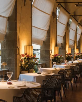A row of linen-topped circular tables on a lamplit open-air restaurant terrace