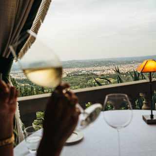 In soft-focus foreground, a guest of La Loggia raises a glass of white wine at a table overlooking Florence's pretty sprawl.