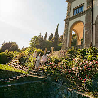 Three guests descend the steps from Villa San Michele to the gardens, in a view that captures pink blooming border shrubs.