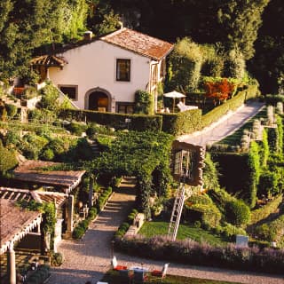 The Limonaia Suite sits in a bowl of lush green, with a deep forest backdrop and pretty gardens all around, seen from above.