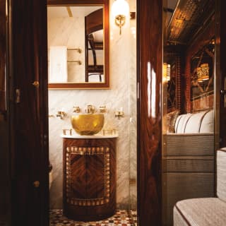 Train cabin bathroom with ornate gold-plated sink and marble-tiled walls
