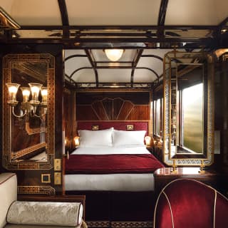 Glass wall lights are reflected in marquetry-edged mirrors. Invitingly crisp white bedlinens are topped with a rich red throw