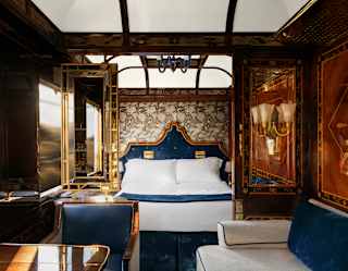 View through Venice Suite's living area and gilt-framed mirror partitions to a bedroom with white bedding and navy headboard.