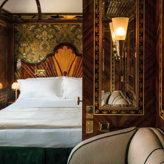 Delicate marquetry surrounds a mirror. An art deco pattern fans out over the bedhead. Gold and green wallpaper fills the walls