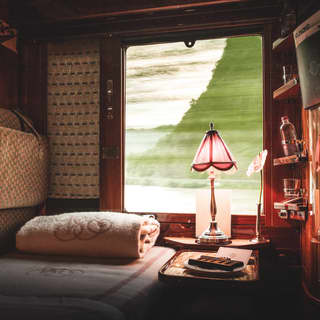 Cosy bed in a lamplit train cabin suite with views through a large window beyond
