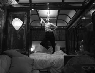 With an air of naughty defiance a woman stands on her unmade bed, leaning on the curving arch of the ceiling panel