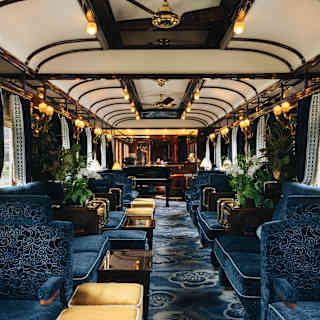 A view through the decadent old-world Bar Car with banquettes and carpet in midnight blue with gold stools and glowing lamps.