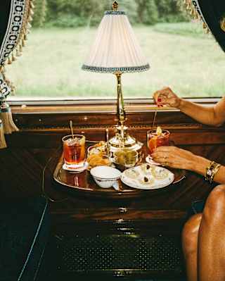 In the Bar Car, a woman with bare legs, mainly off-camera, stirs a Negroni cocktail at a table with aperitifs and nibbles.