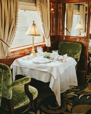 Luxury train dining car with garden-green velvet seating and crystalware on linen-coated tables