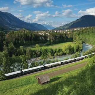 Blue and cream train carriages curving across a sunny Alpine valley