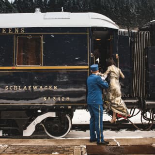 Train steward in a blue uniform helping a lady step up into a blue train carriage