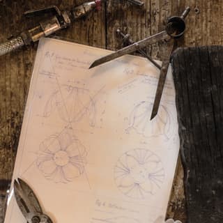 A fluted tulip of white blown glass, callipers and shears hold down artfully drawn plans for a cabbage-shape bowl