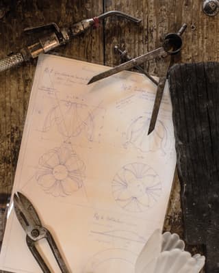 A fluted tulip of white blown glass, callipers and shears hold down artfully drawn plans for a cabbage-shape bowl