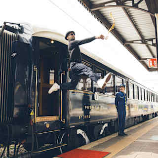 Artist, JR performs a high leap with legs outstretched from train to platform, holding a cup that spills coffee into the air.